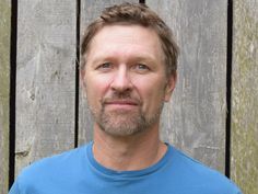 a man wearing a blue shirt standing in front of a wooden fence