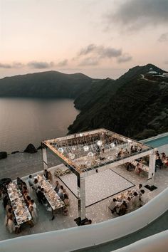 an outdoor dining area overlooking the ocean at dusk with people sitting and standing around it