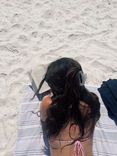 a woman laying on top of a beach next to a book