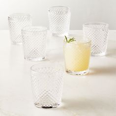 several glasses are lined up next to each other on a counter top, one has a small plant in the middle