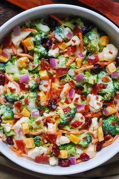 a bowl filled with broccoli, carrots and other vegetables on top of a wooden table