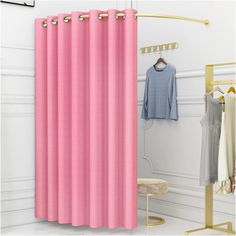 a pink shower curtain hanging next to a white wall with clothes on hangers in front of it