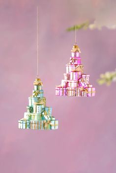 two christmas ornaments hanging from strings with presents on them in front of a pink background