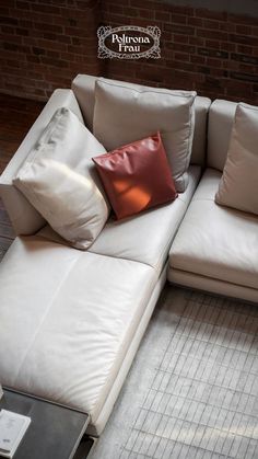 a white couch with pillows on it in front of a brick wall