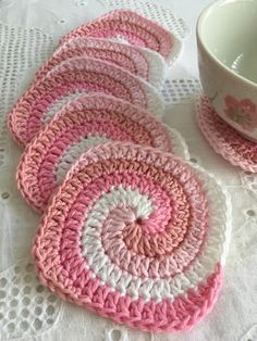 pink and white crocheted coasters on a doily next to a cup