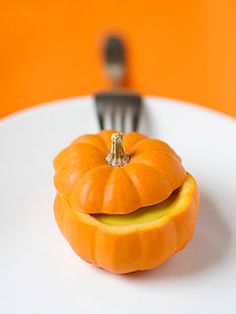 a white plate topped with an orange pumpkin and a fork sticking out of it's mouth