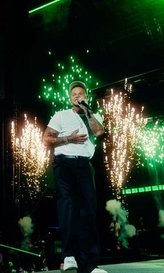 a man standing on top of a stage holding a microphone in his hand and fireworks behind him