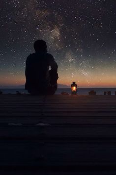 a person sitting on a dock looking at the night sky with stars in the background