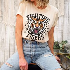 The Fighting Tigers t-shirt is perfect for all the sporting events. This retro and funky tiger tee is everything you've dreamed of and more. This adorable and soft shirt makes a great gift for tiger fans to wear to all the sporting events or just everyday wear! It feels soft and lightweight, with the right amount of stretch. It's comfortable and flattering for all.  Show off your personality with our fun and unique designs!   ** P R O D U C T   D E T A I L S **  - High Quality, Super Soft and Co Graphic Tee For Sports Events With Graphic Print, Sports Season Fan Merchandise Shirt With Graphic Print, Cotton Graphic Tee With Tiger Print, Casual Cotton Tiger Print T-shirt, Casual Cotton T-shirt With Tiger Print, Casual White Tiger Print Top, Short Sleeve Tiger Print Graphic Tee, Tiger Print Short Sleeve Graphic Tee, Tiger Print Crew Neck Graphic Tee