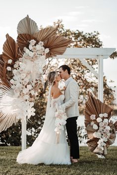 a bride and groom standing under an arch decorated with paper flowers at their wedding ceremony