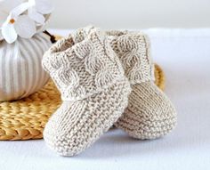 two knitted baby booties sitting on top of a wicker basket next to a white flower