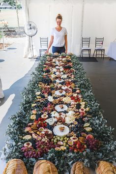 a woman standing in front of a long table filled with fruits and veggies