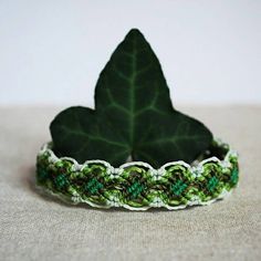 a green and white bracelet sitting on top of a table next to a large leaf