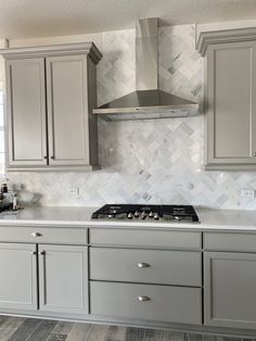 a stove top oven sitting inside of a kitchen next to gray cupboards and drawers