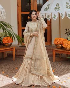 a woman standing in front of an open door wearing a white lehenga with orange flowers