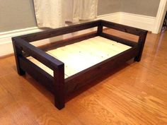 a wooden bed frame sitting on top of a hard wood floor next to a white curtain