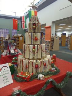 a christmas tree made out of wrapped presents on a red table cloth in a library