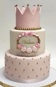 a three tiered cake with pink and white frosting on top, topped with a crown