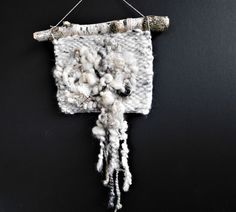 a piece of art made out of yarn hanging from a hook on a black wall