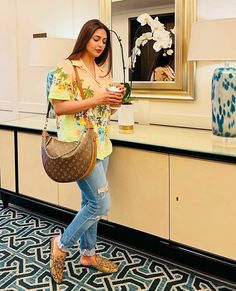 a woman standing in front of a mirror looking at her cell phone and holding a purse