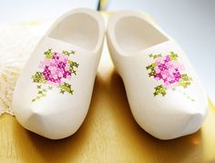 pair of white shoes with pink and green flowers on them sitting on a wooden table