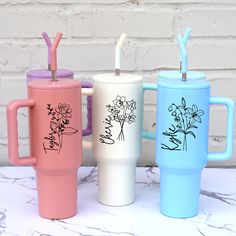 three different colored coffee cups with straws in them sitting next to each other on a table