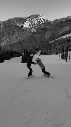 two snowboarders are touching each other in the snow with mountains in the background