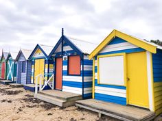 a row of colorful beach huts sitting next to each other on top of a sandy beach