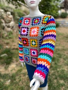 a mannequin wearing a multicolored crochet sweater in the grass