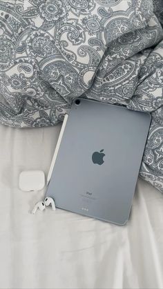 an apple ipad sitting on top of a bed next to headphones and earbuds