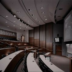 an empty lecture hall with rows of desks and projector screen in the center