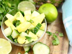 sliced cucumbers and limes in a glass bowl on a cutting board next to chopped cilantro