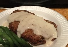 a white plate topped with meat covered in gravy next to green beans and asparagus