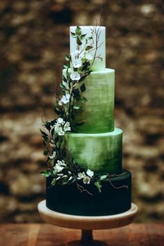 a three tiered green cake with white flowers on the top and bottom, sitting on a wooden table