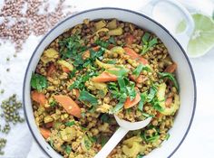 a bowl filled with lentils and carrots next to a glass of limeade