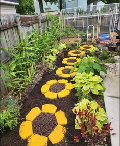 a garden with flowers and plants in the ground next to a fenced in area