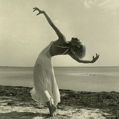 a woman in a white dress is on the beach with her arms stretched out and legs extended