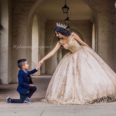 a young boy kneeling down next to a woman in a ball gown and holding her hand