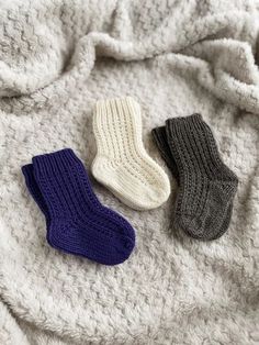 two pairs of socks laying on top of a white and gray blanket next to each other