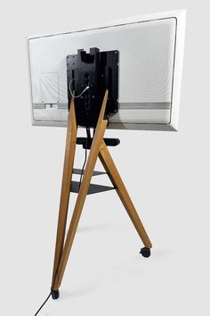 a wooden tripod stands next to a computer monitor on a white surface with a black clock in the center