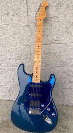 a blue electric guitar sitting on top of a cement floor next to a white wall