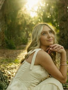 a woman sitting on the ground in front of a tree with her hand under her chin