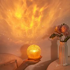 a person holding a light in their hand with flowers on the table next to it