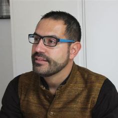 a man with glasses sitting in front of a white door and looking at the camera