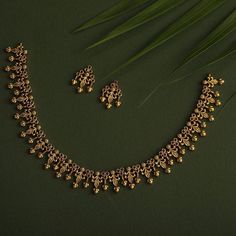 a gold necklace and earring set on a green surface with palm leaves in the background