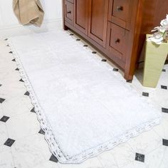 a white rug in a bathroom next to a wooden cabinet and toilet paper dispenser