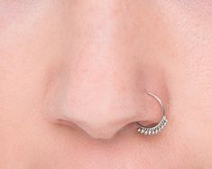 a woman's nose with a silver nose ring on top of her nose and an ear piercing in the middle