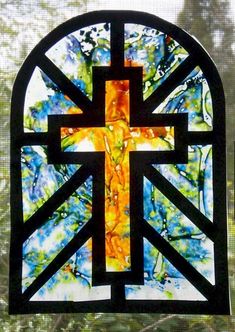 a stained glass window with a cross in the center and trees behind it, on a sunny day