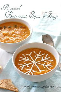 two bowls of roasted butternut squash soup with crackers and spoons on the side