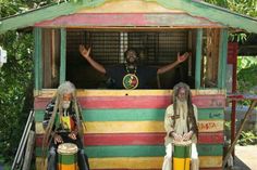 two men with dreadlocks sitting in front of a colorful bus